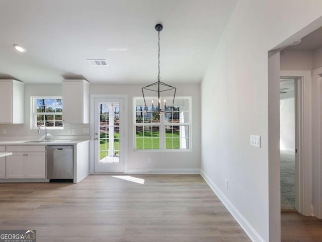 kitchen featuring pendant lighting, white cabinets, stainless steel dishwasher, light wood-type flooring, and a notable chandelier