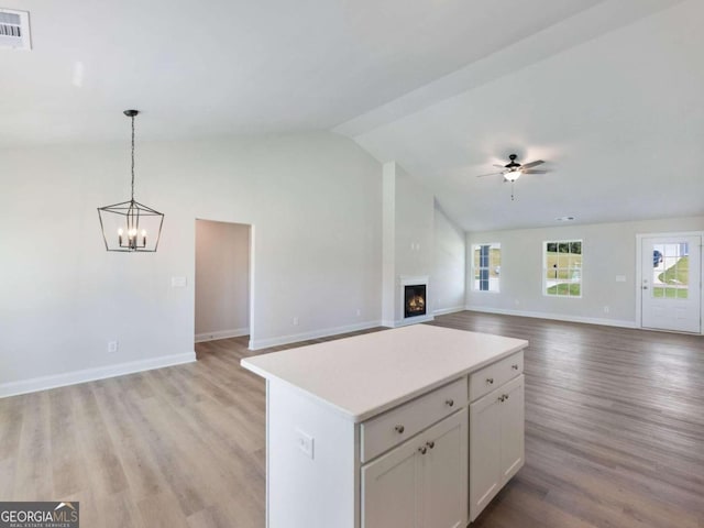 kitchen featuring ceiling fan with notable chandelier, white cabinets, light hardwood / wood-style floors, a kitchen island, and lofted ceiling