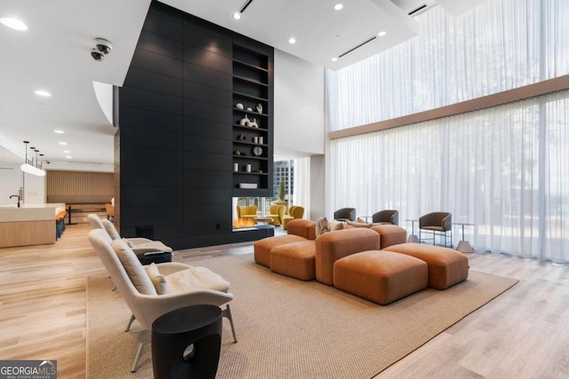 living room featuring built in shelves, plenty of natural light, light hardwood / wood-style flooring, and a high ceiling