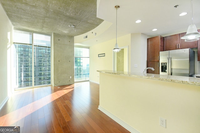 kitchen with light stone countertops, stainless steel fridge, decorative light fixtures, and dark wood-type flooring