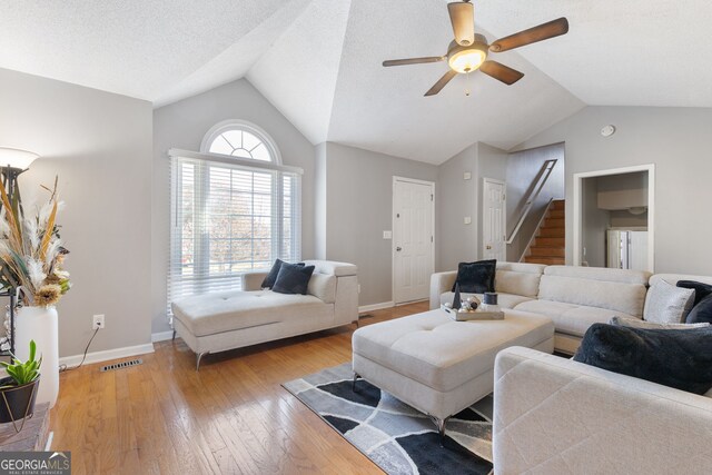 living room featuring a brick fireplace, a textured ceiling, vaulted ceiling, ceiling fan, and light hardwood / wood-style flooring