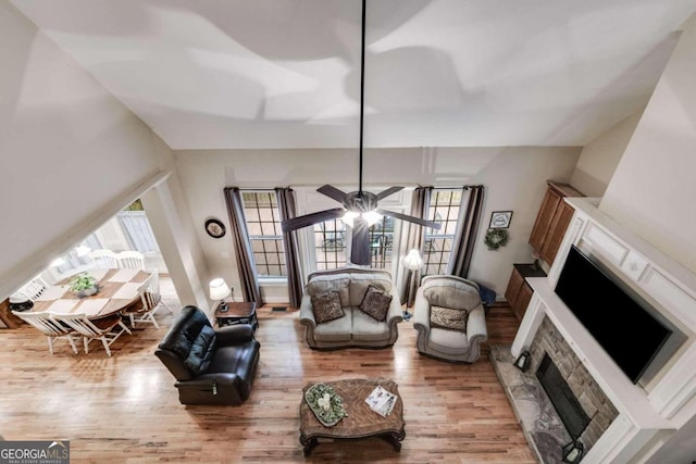 living room with ceiling fan, a stone fireplace, and light wood-type flooring