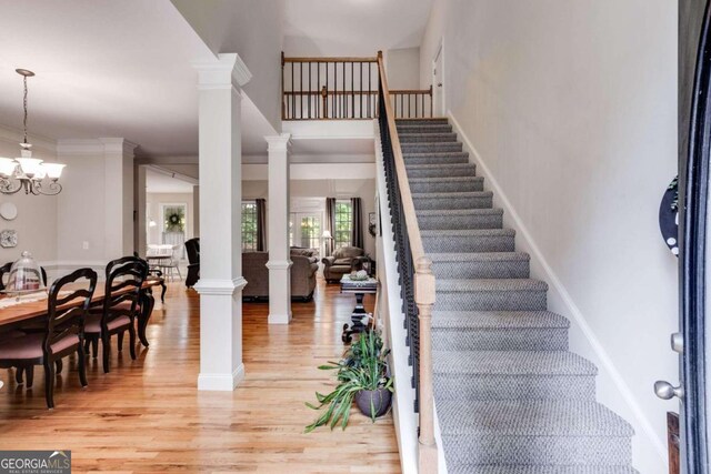 entrance foyer with ornate columns, light wood-type flooring, crown molding, and a chandelier