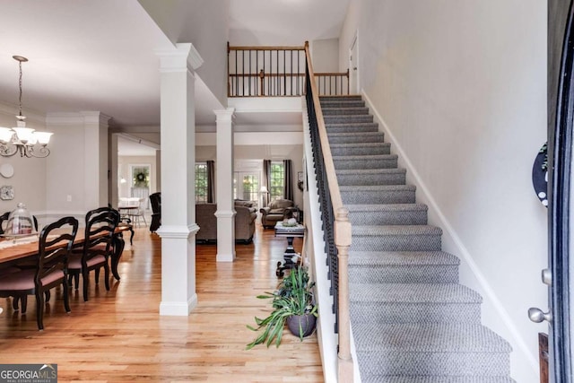 entrance foyer with crown molding, a chandelier, light wood-type flooring, and ornate columns