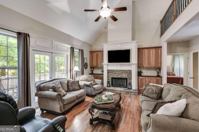 living room with ceiling fan, light hardwood / wood-style floors, a fireplace, and high vaulted ceiling