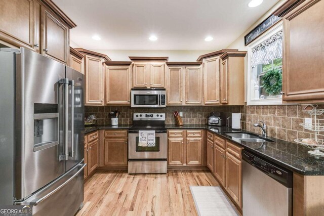 kitchen with sink, light hardwood / wood-style flooring, decorative backsplash, dark stone countertops, and appliances with stainless steel finishes