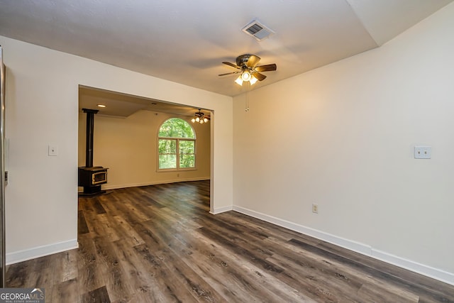 spare room with dark hardwood / wood-style floors, ceiling fan, and a wood stove