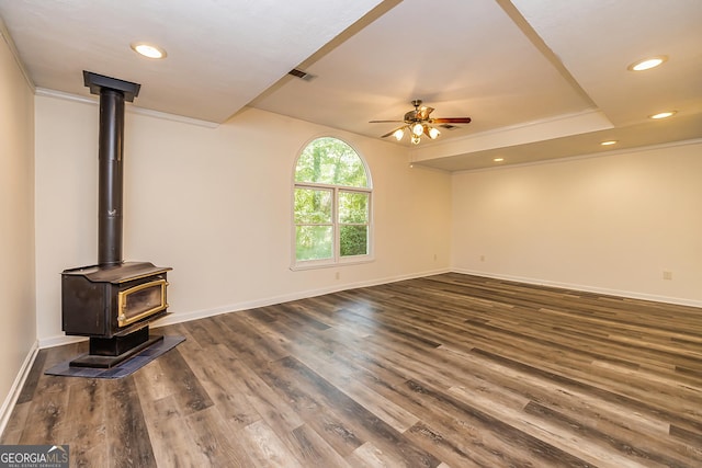 unfurnished living room featuring ceiling fan, dark hardwood / wood-style flooring, a wood stove, and crown molding