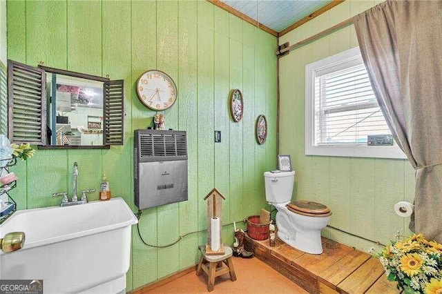 bathroom with toilet, sink, wooden walls, and heating unit