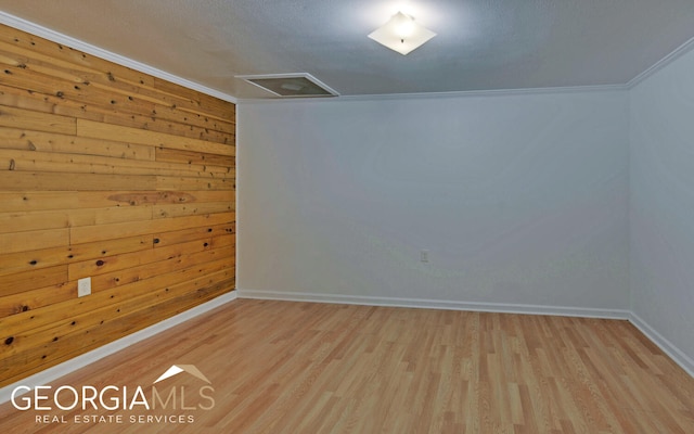 spare room featuring light hardwood / wood-style flooring, wooden walls, and crown molding