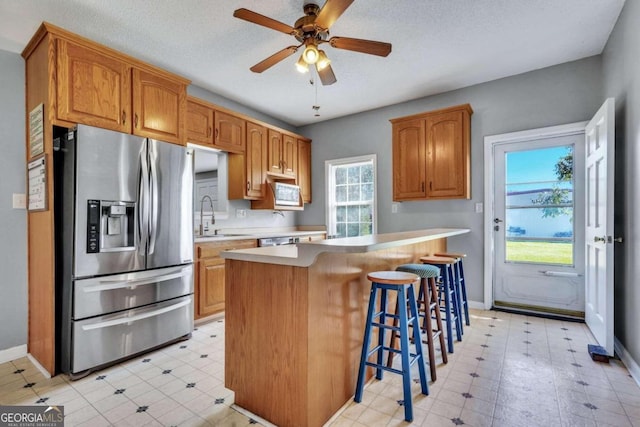 kitchen featuring a center island, a kitchen breakfast bar, sink, stainless steel refrigerator with ice dispenser, and a textured ceiling