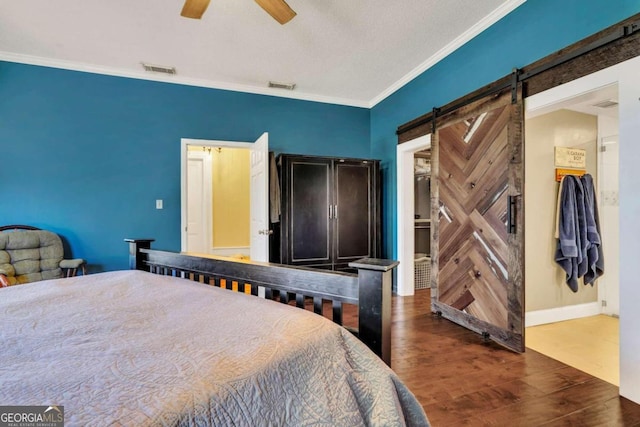 bedroom featuring a walk in closet, ornamental molding, ceiling fan, a barn door, and dark hardwood / wood-style floors