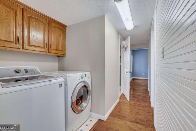 laundry area featuring washer and clothes dryer, cabinets, a textured ceiling, and light wood-type flooring