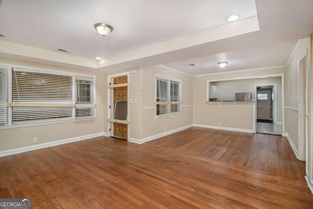 unfurnished living room with hardwood / wood-style flooring, a raised ceiling, and crown molding