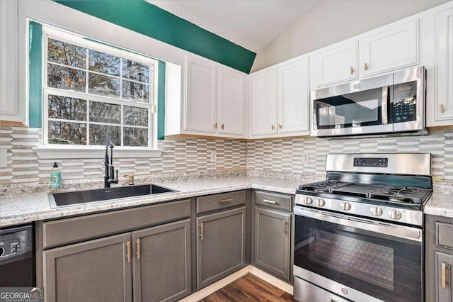 kitchen with lofted ceiling, sink, gray cabinets, appliances with stainless steel finishes, and white cabinetry