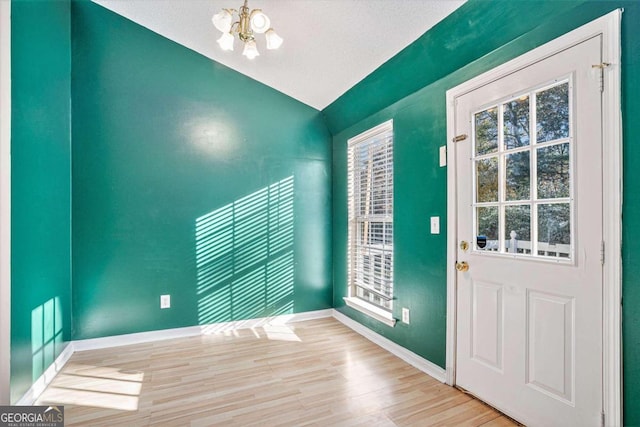 entryway featuring a chandelier, vaulted ceiling, a textured ceiling, and light hardwood / wood-style flooring