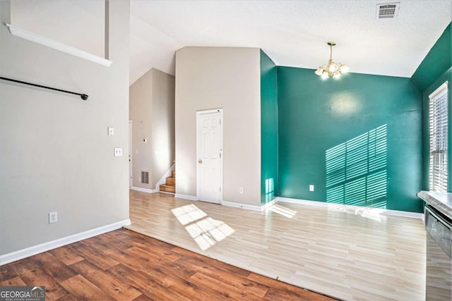 spare room featuring hardwood / wood-style floors, high vaulted ceiling, a textured ceiling, and an inviting chandelier