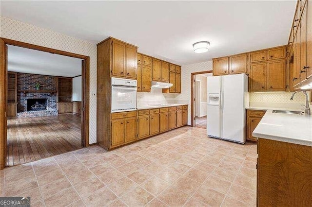 kitchen featuring backsplash, sink, white appliances, and a brick fireplace