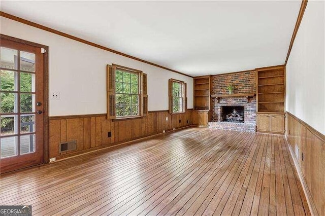 unfurnished living room with a fireplace, hardwood / wood-style floors, built in features, and crown molding