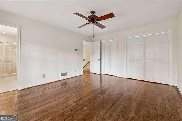 unfurnished bedroom with ensuite bathroom, dark hardwood / wood-style flooring, ceiling fan, and two closets