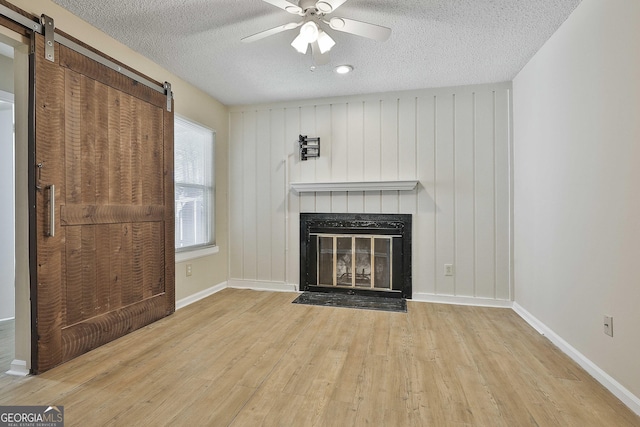 unfurnished living room featuring a textured ceiling, ceiling fan, light hardwood / wood-style floors, and a barn door