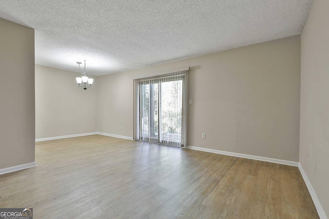 unfurnished room with a textured ceiling, light hardwood / wood-style flooring, and an inviting chandelier