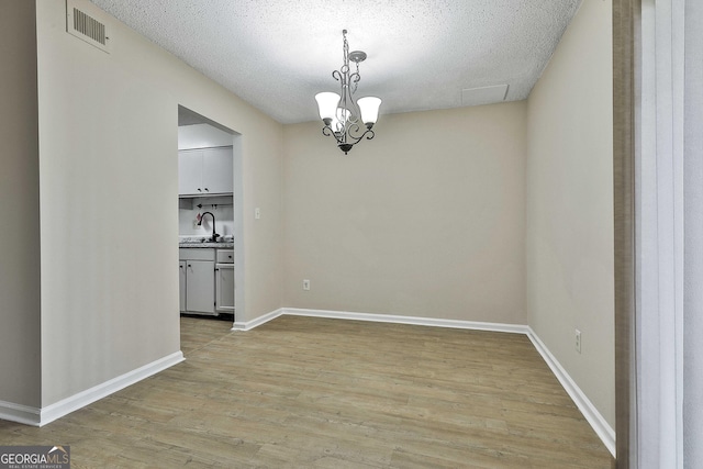 unfurnished dining area with sink, a textured ceiling, light hardwood / wood-style flooring, and a chandelier