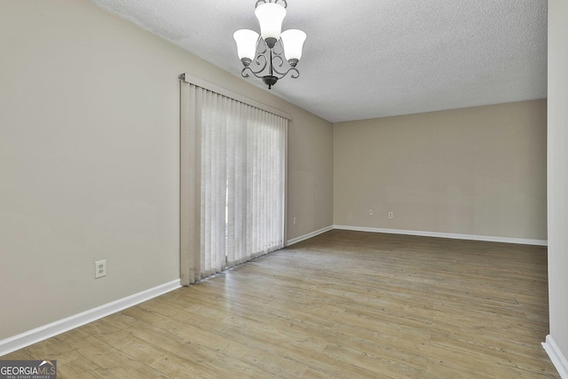 empty room with light wood-type flooring, a notable chandelier, and a textured ceiling