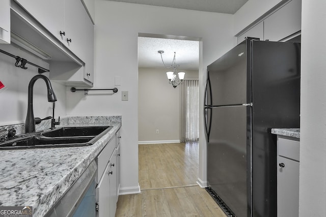 kitchen with black refrigerator, decorative light fixtures, light wood-type flooring, a chandelier, and sink