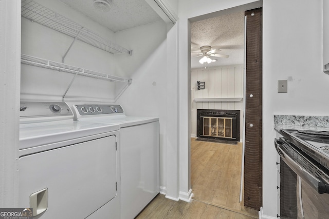 clothes washing area featuring a textured ceiling, ceiling fan, washer and dryer, and light wood-type flooring