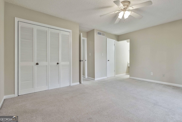 unfurnished bedroom with ceiling fan, light carpet, a closet, and a textured ceiling