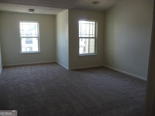 spare room with a textured ceiling, dark carpet, and plenty of natural light