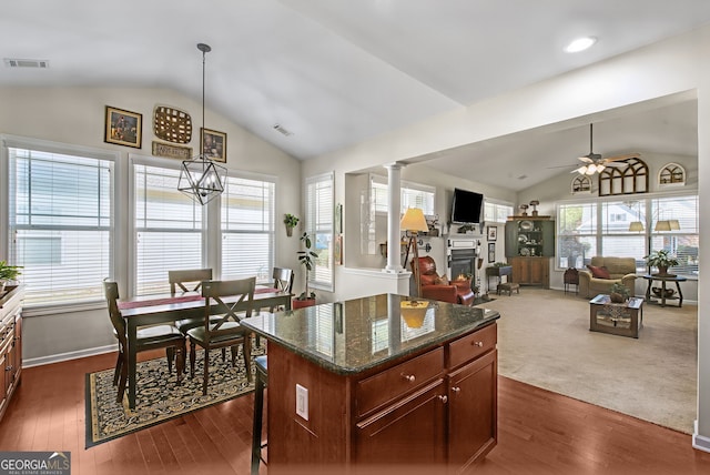 kitchen with decorative columns, ceiling fan, dark wood-type flooring, dark stone countertops, and lofted ceiling