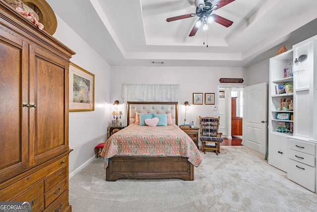 bedroom with a tray ceiling, ceiling fan, and light carpet