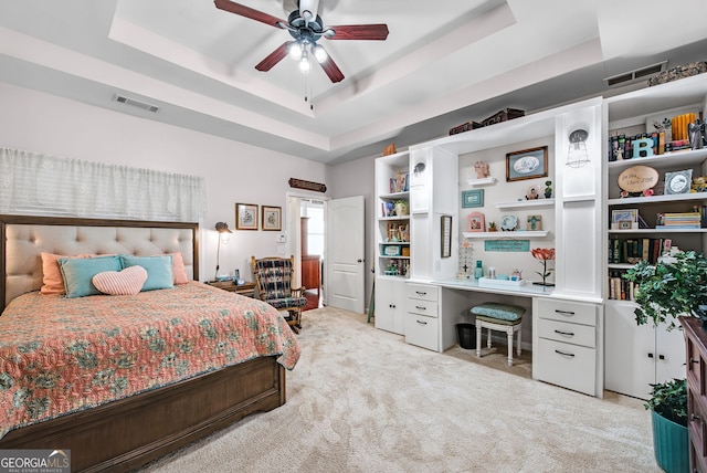 bedroom featuring ceiling fan, light colored carpet, and a tray ceiling