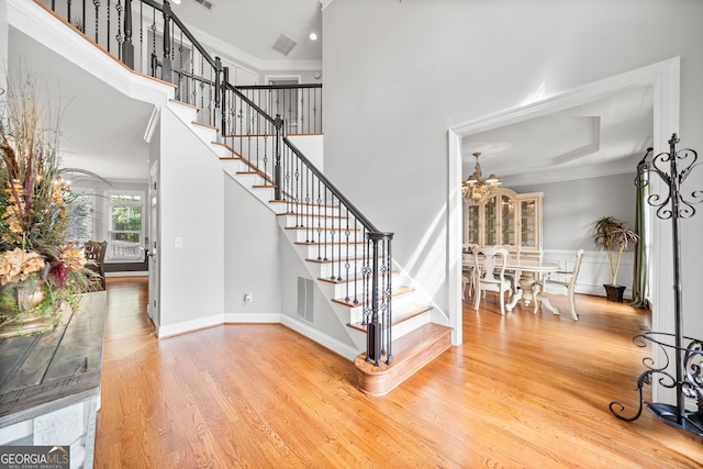 staircase featuring a towering ceiling, ornamental molding, and hardwood / wood-style flooring