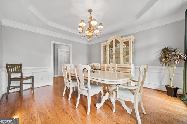 dining space with light wood-type flooring, crown molding, and a notable chandelier