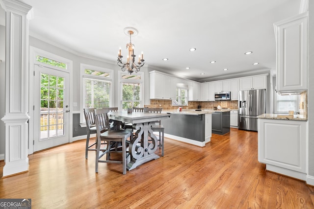 dining space featuring light wood-type flooring, an inviting chandelier, ornate columns, and crown molding