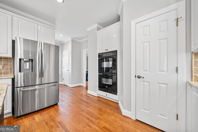 kitchen featuring backsplash, stainless steel refrigerator with ice dispenser, black double oven, light hardwood / wood-style floors, and white cabinetry