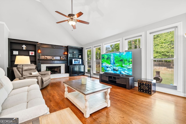 living room featuring a brick fireplace, high vaulted ceiling, a healthy amount of sunlight, and wood-type flooring