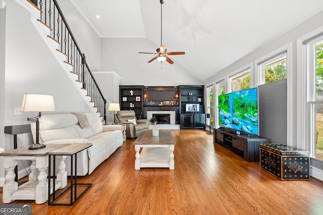 living room with ceiling fan, light hardwood / wood-style flooring, high vaulted ceiling, and a brick fireplace