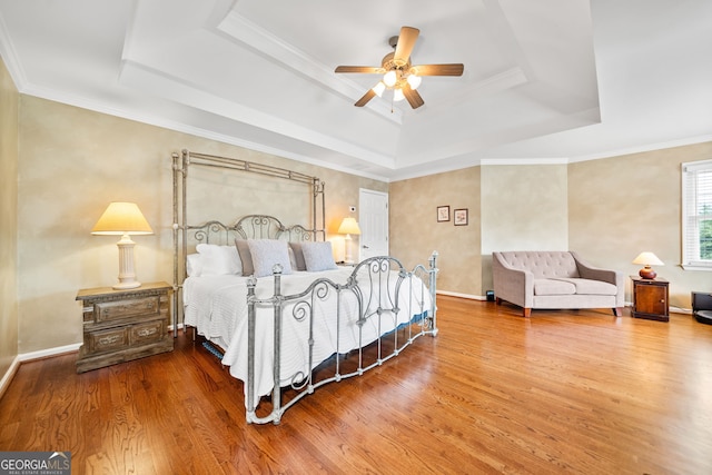 bedroom featuring wood-type flooring, a tray ceiling, ceiling fan, and ornamental molding