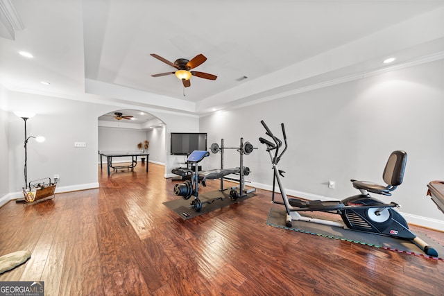 exercise area featuring a tray ceiling, crown molding, ceiling fan, and dark wood-type flooring