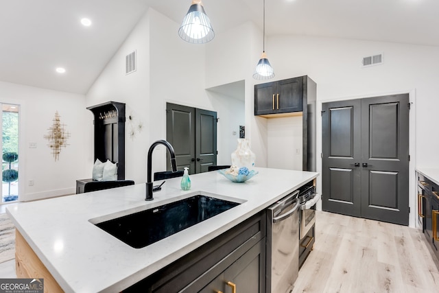 kitchen with pendant lighting, a kitchen island with sink, sink, light hardwood / wood-style flooring, and light stone countertops