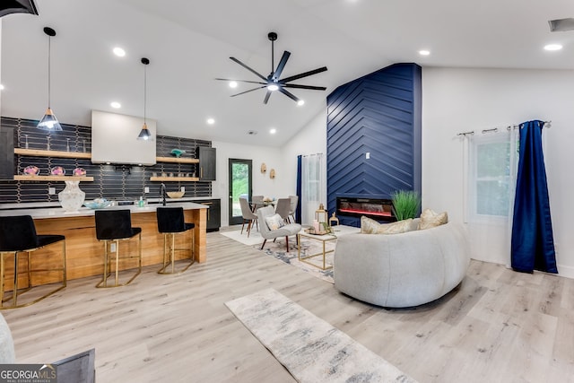 living room featuring ceiling fan, a fireplace, vaulted ceiling, and light hardwood / wood-style flooring