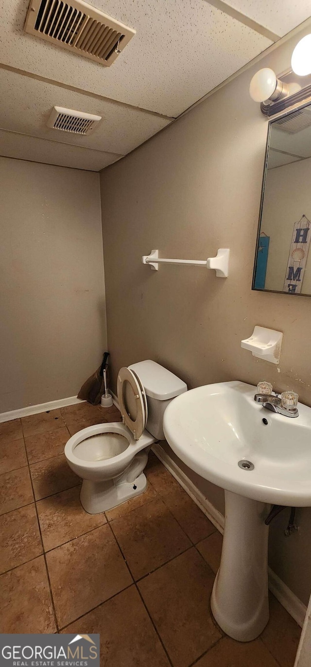 bathroom featuring tile patterned flooring, a drop ceiling, and toilet