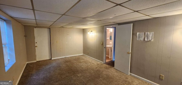 unfurnished room featuring carpet flooring, a paneled ceiling, and wooden walls