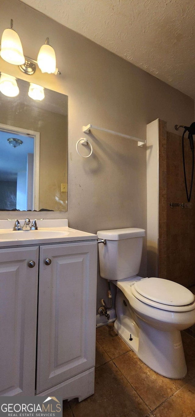 bathroom featuring a tile shower, a textured ceiling, vanity, tile patterned flooring, and toilet