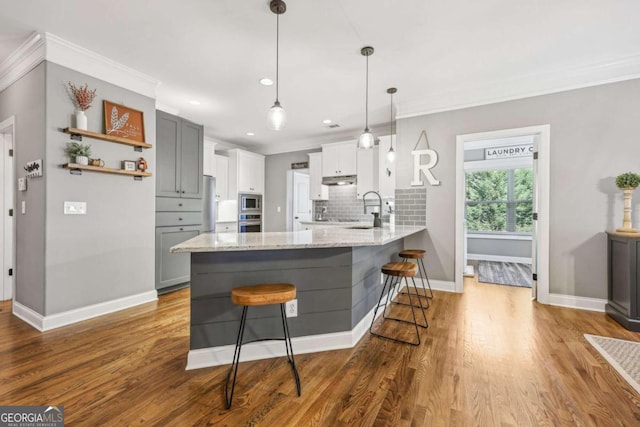 kitchen featuring gray cabinetry, tasteful backsplash, kitchen peninsula, wood-type flooring, and a kitchen bar