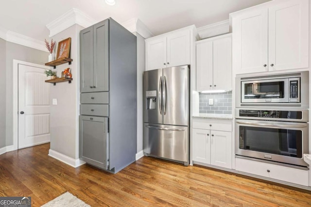 kitchen featuring appliances with stainless steel finishes, tasteful backsplash, crown molding, wood-type flooring, and white cabinets